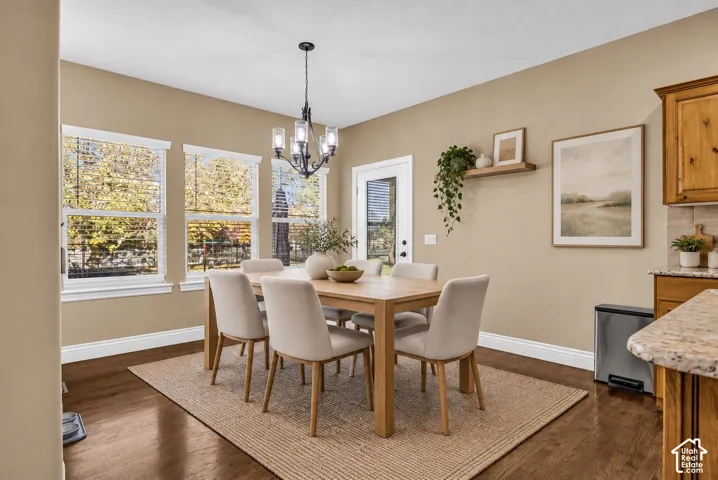 Dining area featuring wood-finish flooring, multi-pane windows, a decorative chandelier, a wall-mounted wood shelf, and natural-finish wood cabinetry with stone-finish countertops