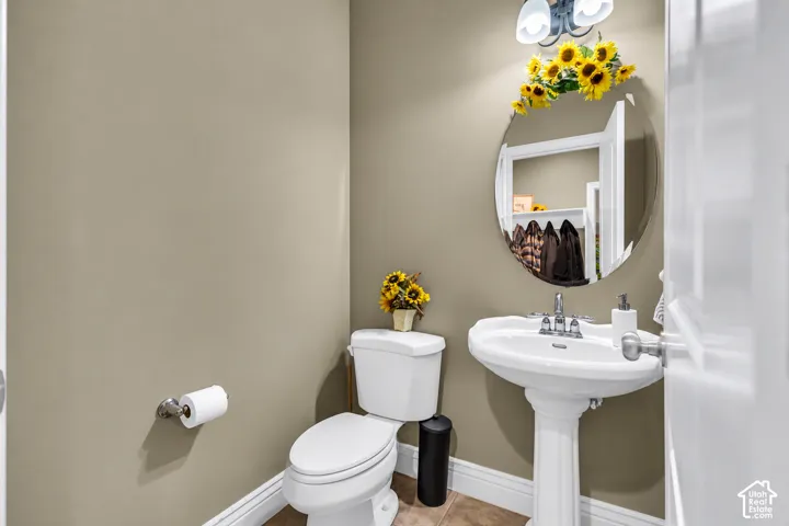 Pedestal sink with a dual-handle chrome faucet, wall-mounted oval mirror, and two-light vanity fixture