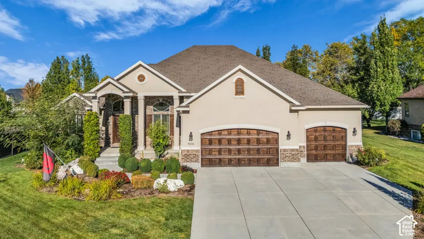 Exterior featuring a stucco and brick facade, arched wood-finish garage doors, concrete driveway, and covered entryway with columns
