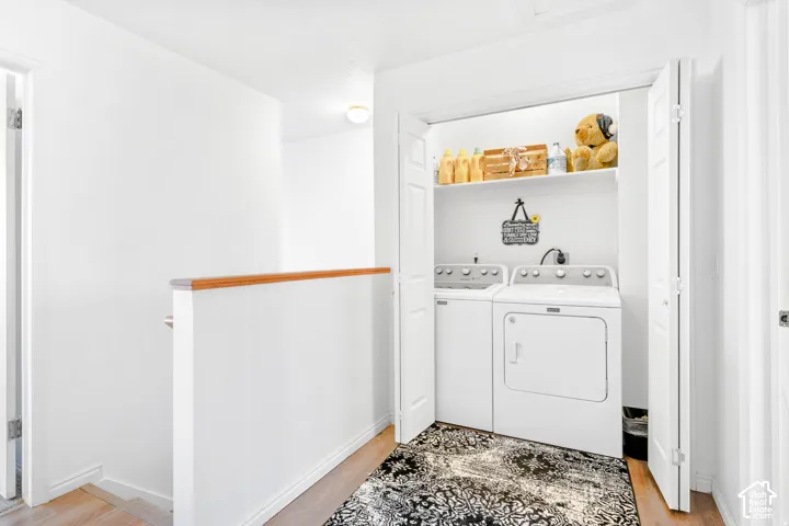 Laundry closet featuring bi-fold doors and integrated shelving, complemented by wood-finish flooring and a partial wall with a wood-finished handrail