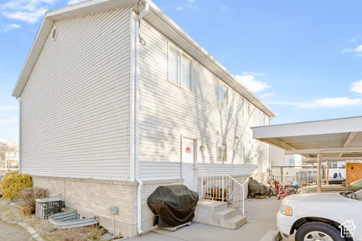 Multi-level residential exterior featuring light-colored horizontal siding, a masonry foundation, a concrete patio, and a covered parking structure