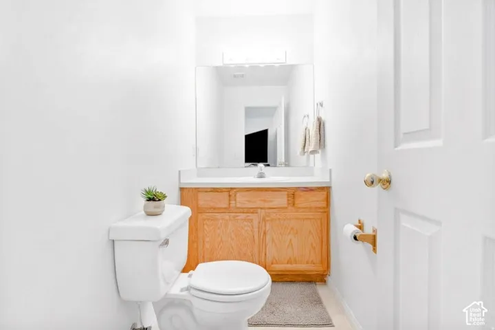 Wood-finish cabinetry featuring a light-toned wood grain, white countertop with an integrated sink, full-width mirror, and polished metal hardware