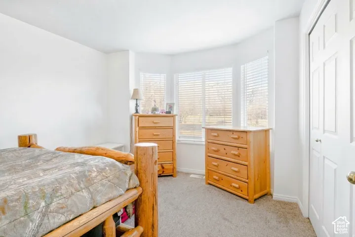 Neutral-toned carpeting, bay window with horizontal blinds, and a closet with bifold doors
