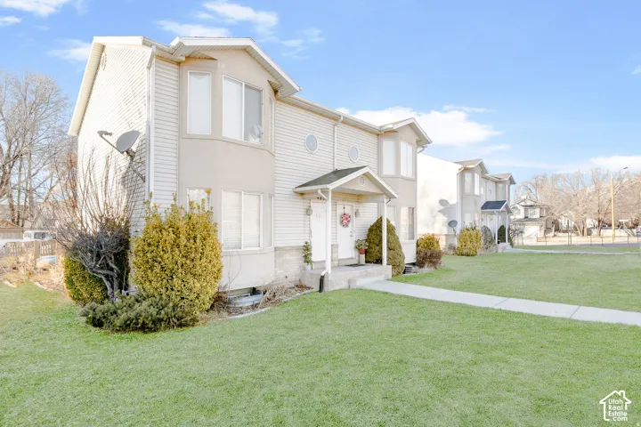 Two-story townhouse exterior featuring vinyl siding, bay windows, circular accent windows, and a covered front entryway with a concrete stoop