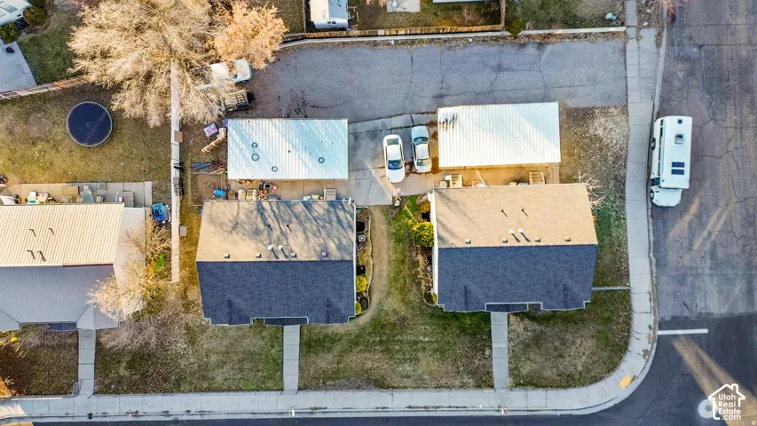 Aerial perspective of a residential lot featuring dual metal-roofed carports, paved driveway surfaces, and concrete walkways