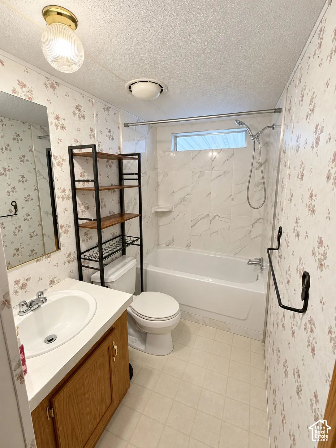Bathroom featuring a vanity with a white countertop and oval basin, a shower-tub combination with white tile-patterned surround, and an integrated transom window