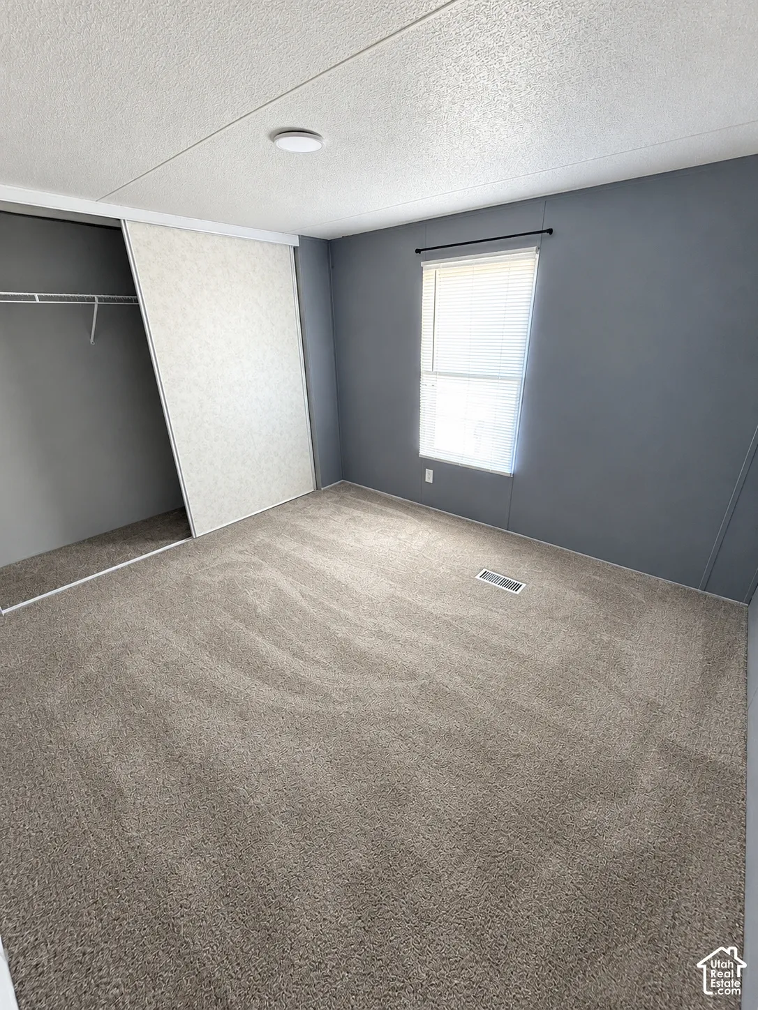 Neutral-toned wall paint, neutral carpeting, sliding closet door, and window with attached blinds