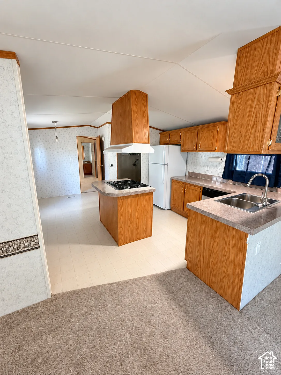 Kitchen featuring wood cabinetry, a center island with a cooktop, a range hood, and double-basin stainless steel sink