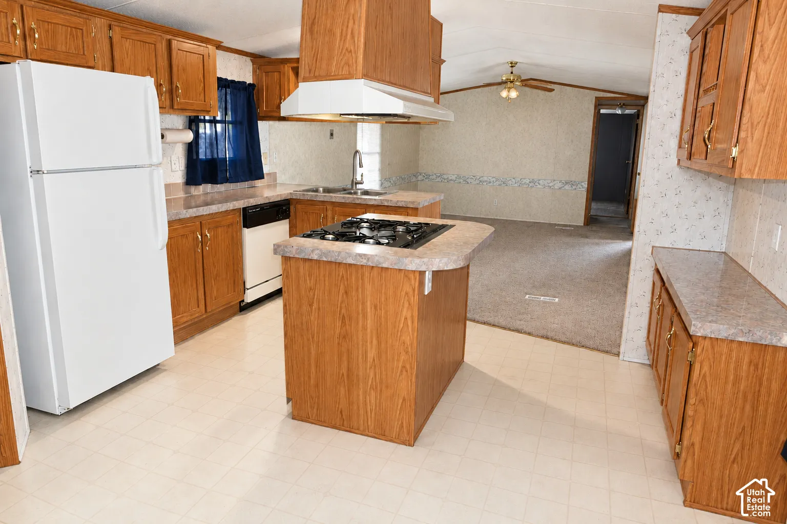 Kitchen featuring wood cabinetry, laminate countertops, a center island with an integrated cooktop, and an overhead range hood