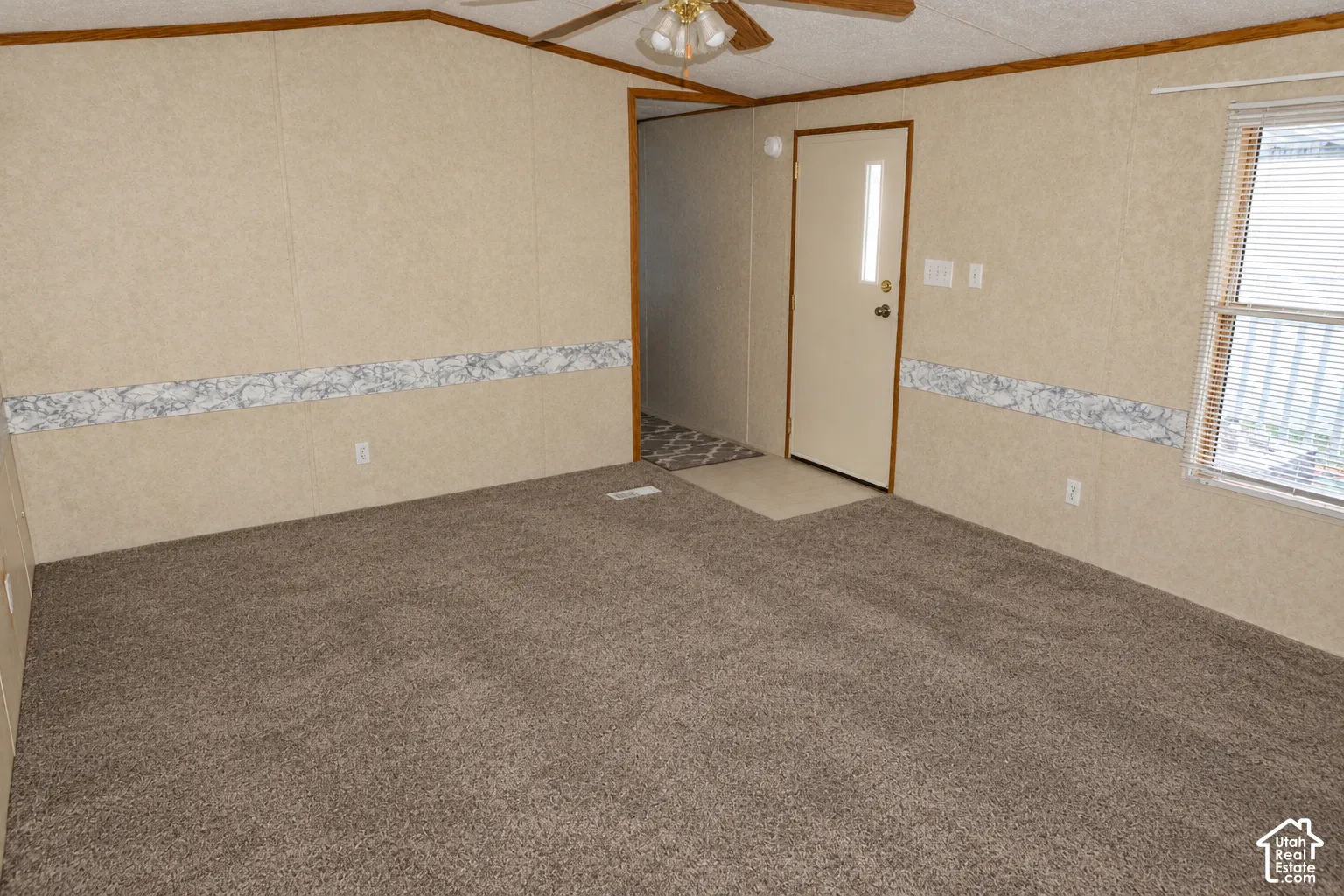 Interior space featuring wall-to-wall carpeting, wood-tone ceiling trim, a ceiling fan with integrated lighting, and a single-light entry door
