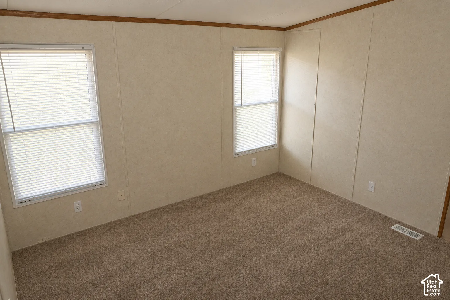 Room featuring wall-to-wall carpeting, two windows with horizontal blinds, and neutral-tone wall paneling