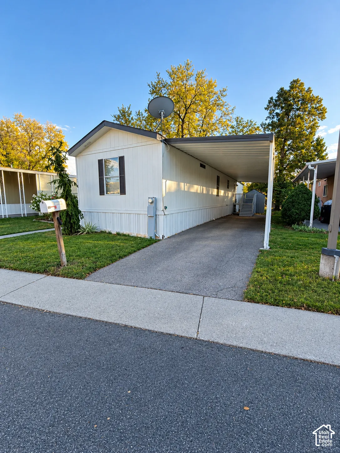 White exterior siding with an attached metal carport, asphalt driveway, and green lawn