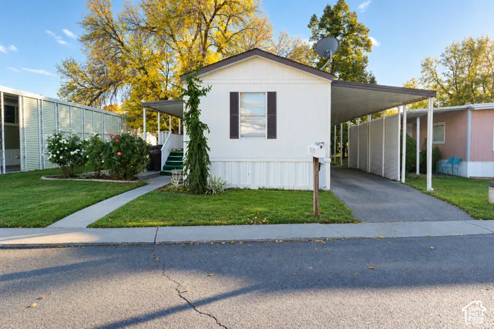 White exterior siding featuring dark-trimmed window shutters, an attached metal carport, and concrete walkway