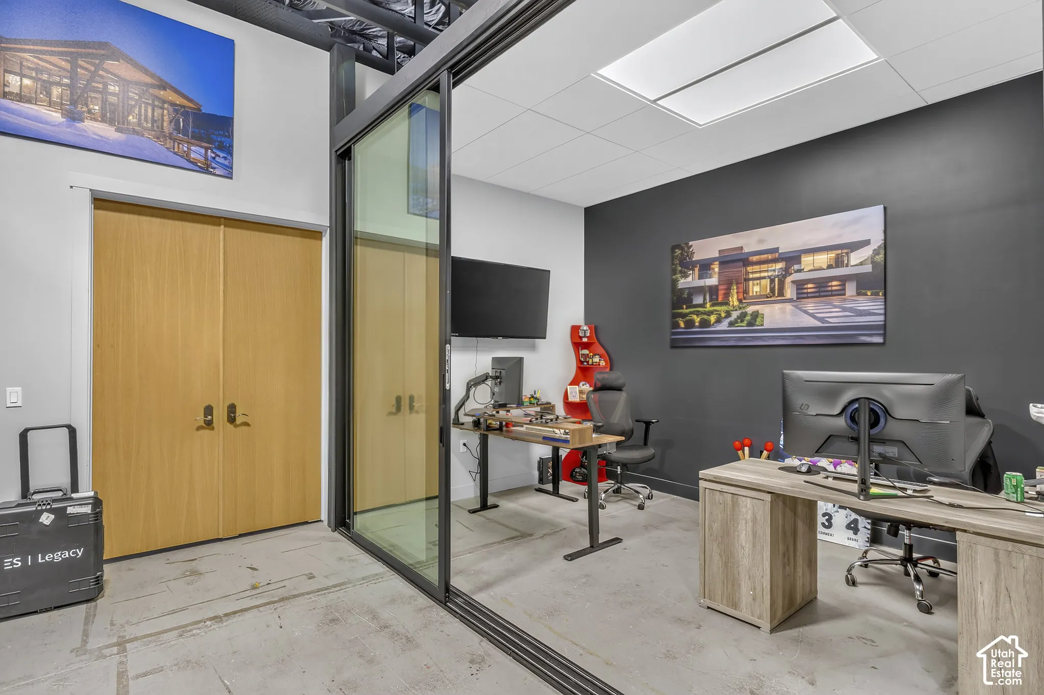 Glass sliding partition with a dark metal frame, double wood-veneer doors, exposed ceiling structure, recessed square lighting, and a charcoal-toned accent wall