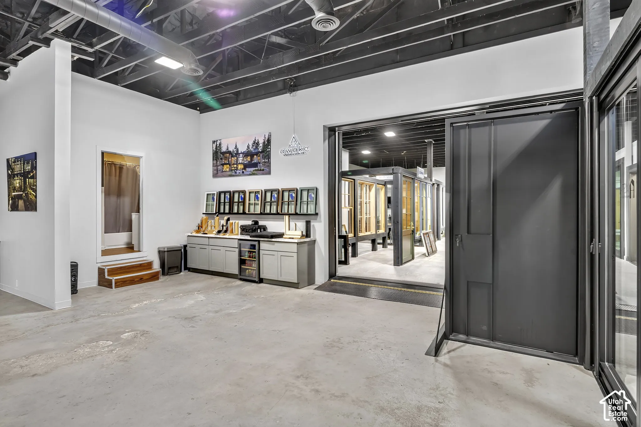 Industrial-style space featuring exposed painted ceiling, polished concrete flooring, built-in cabinetry with integrated under-counter refrigeration, and a large-format metal sliding door system
