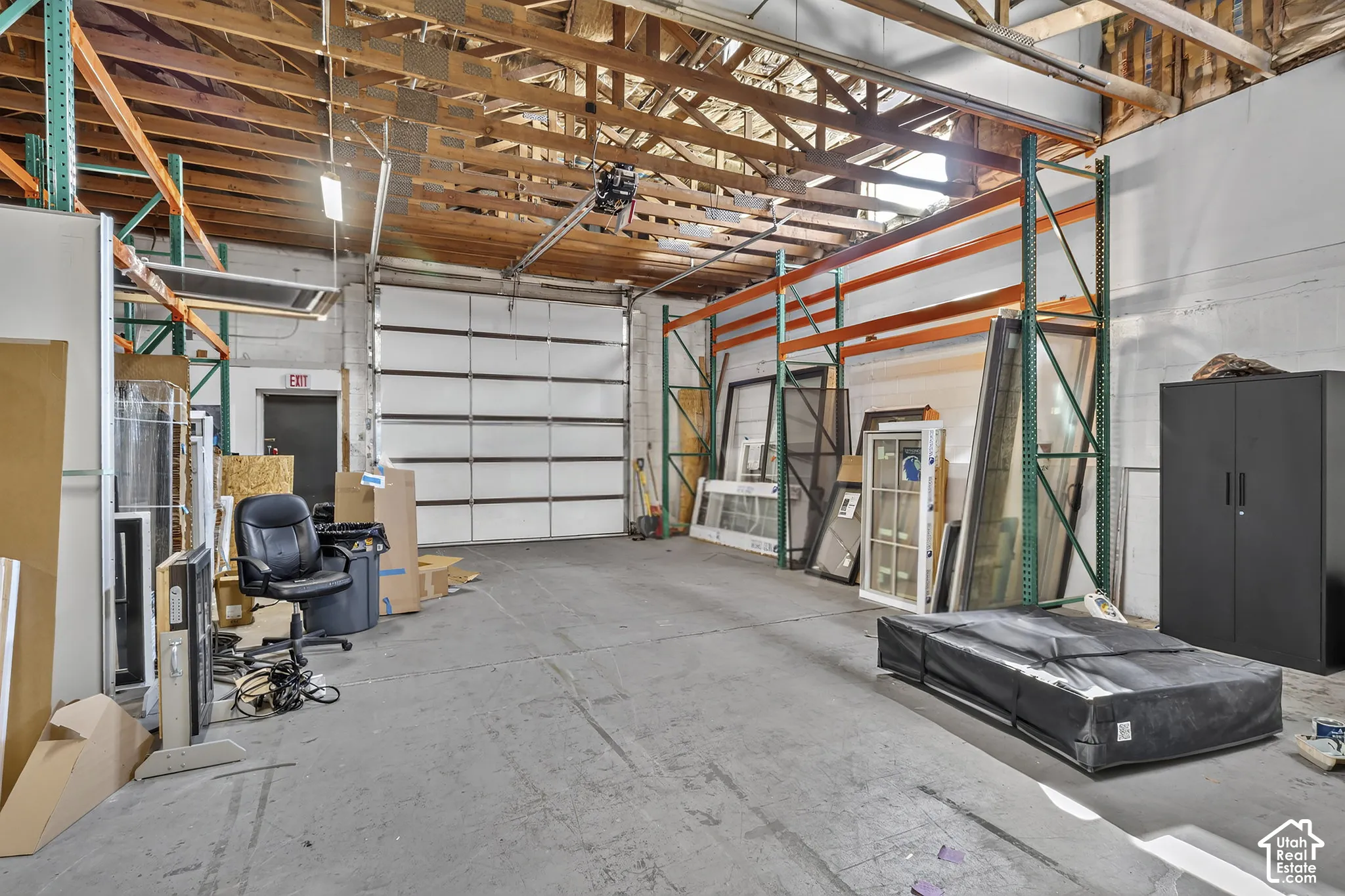 Industrial warehouse space featuring high vaulted ceilings with exposed wood trusses, concrete flooring, and a large sectional roll-up door