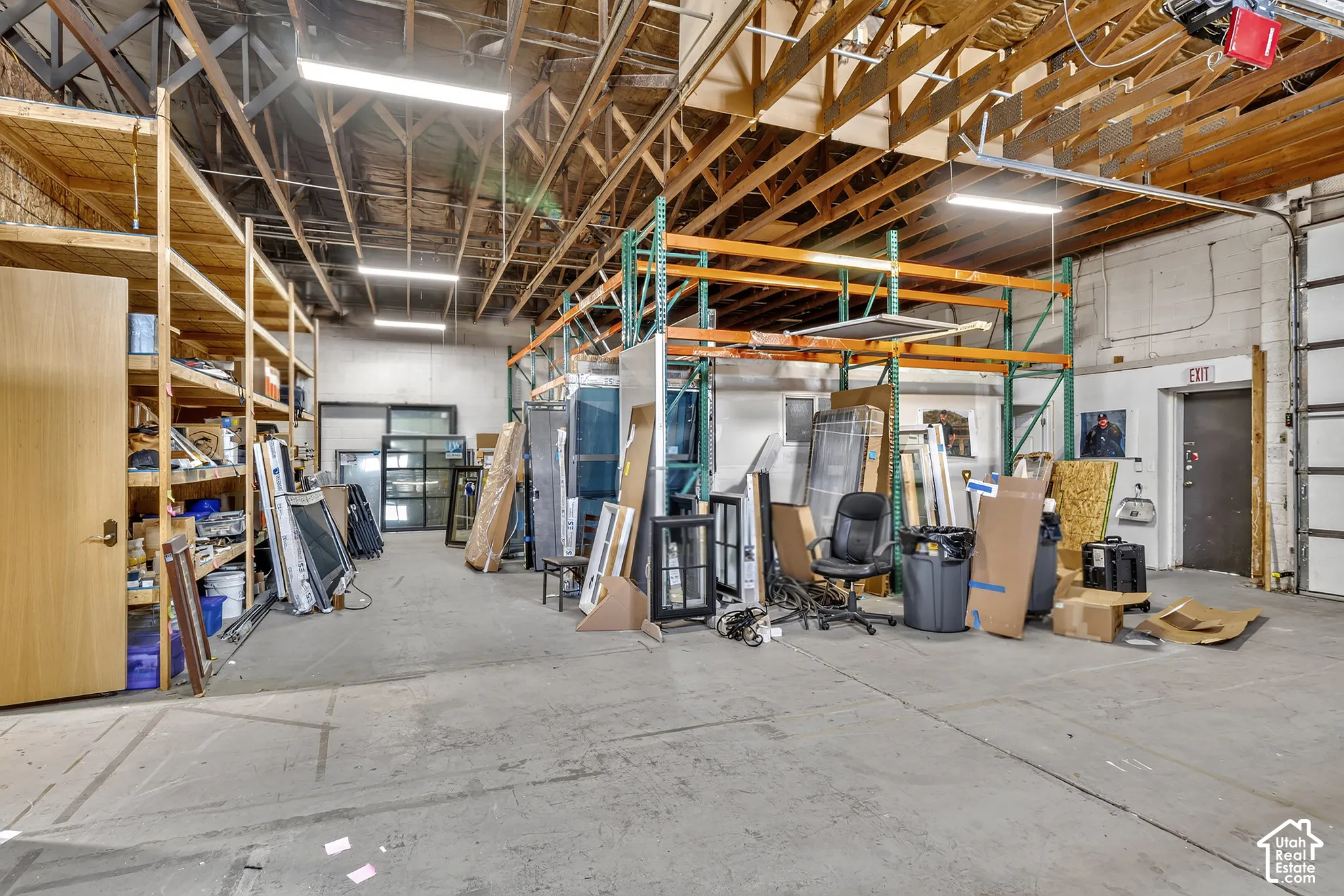 Industrial warehouse space featuring exposed timber truss ceilings, concrete flooring, high-clearance overhead lighting, and built-in steel shelving units