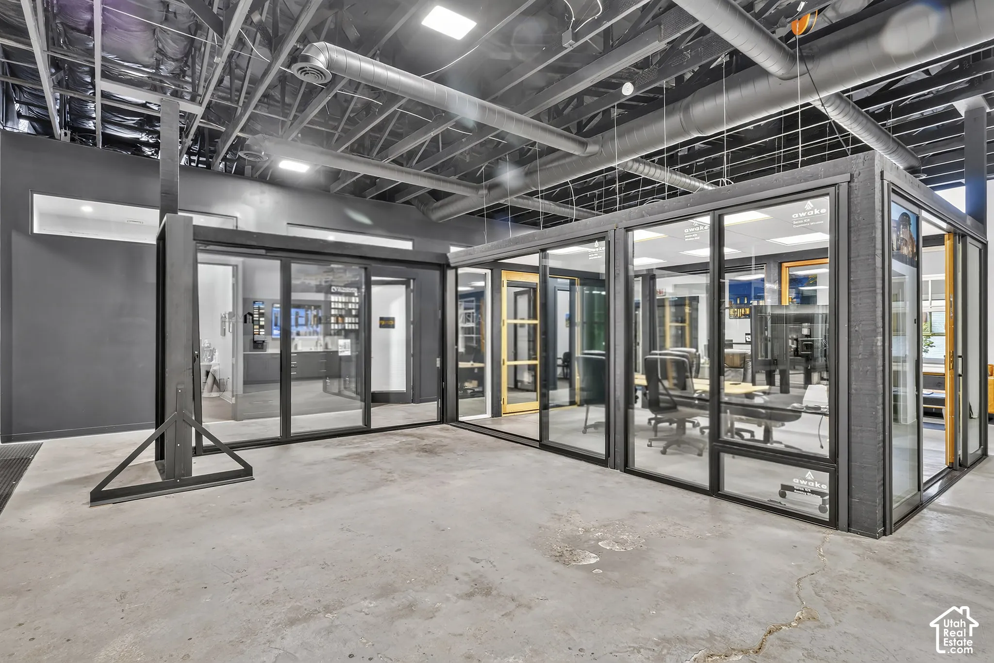 Industrial-style interior featuring an exposed ceiling with open ductwork, polished concrete flooring, and modular glass-paneled enclosures with black metal framing
