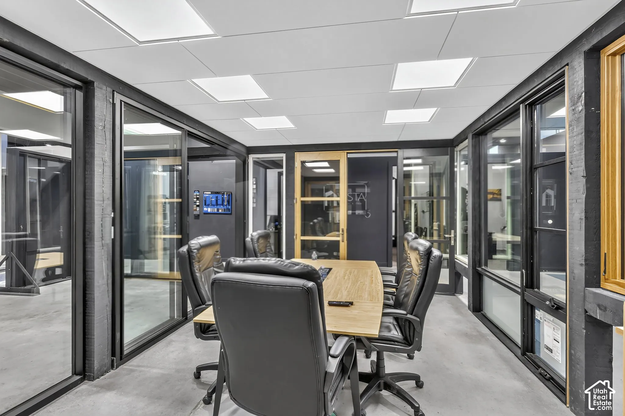 Polished concrete flooring, expansive glass wall partitions with black frames, recessed square ceiling lighting, and natural wood trim accents