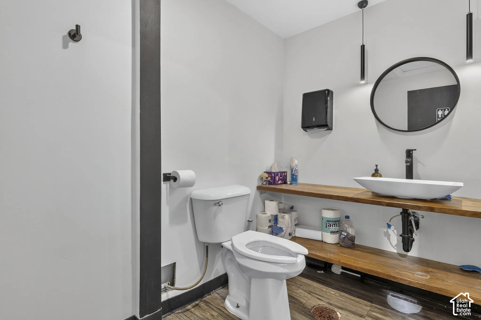 Bathroom featuring wood-finish flooring, dual-tier open wood shelving, a white vessel sink, matte black faucet, and a round wall-mounted mirror