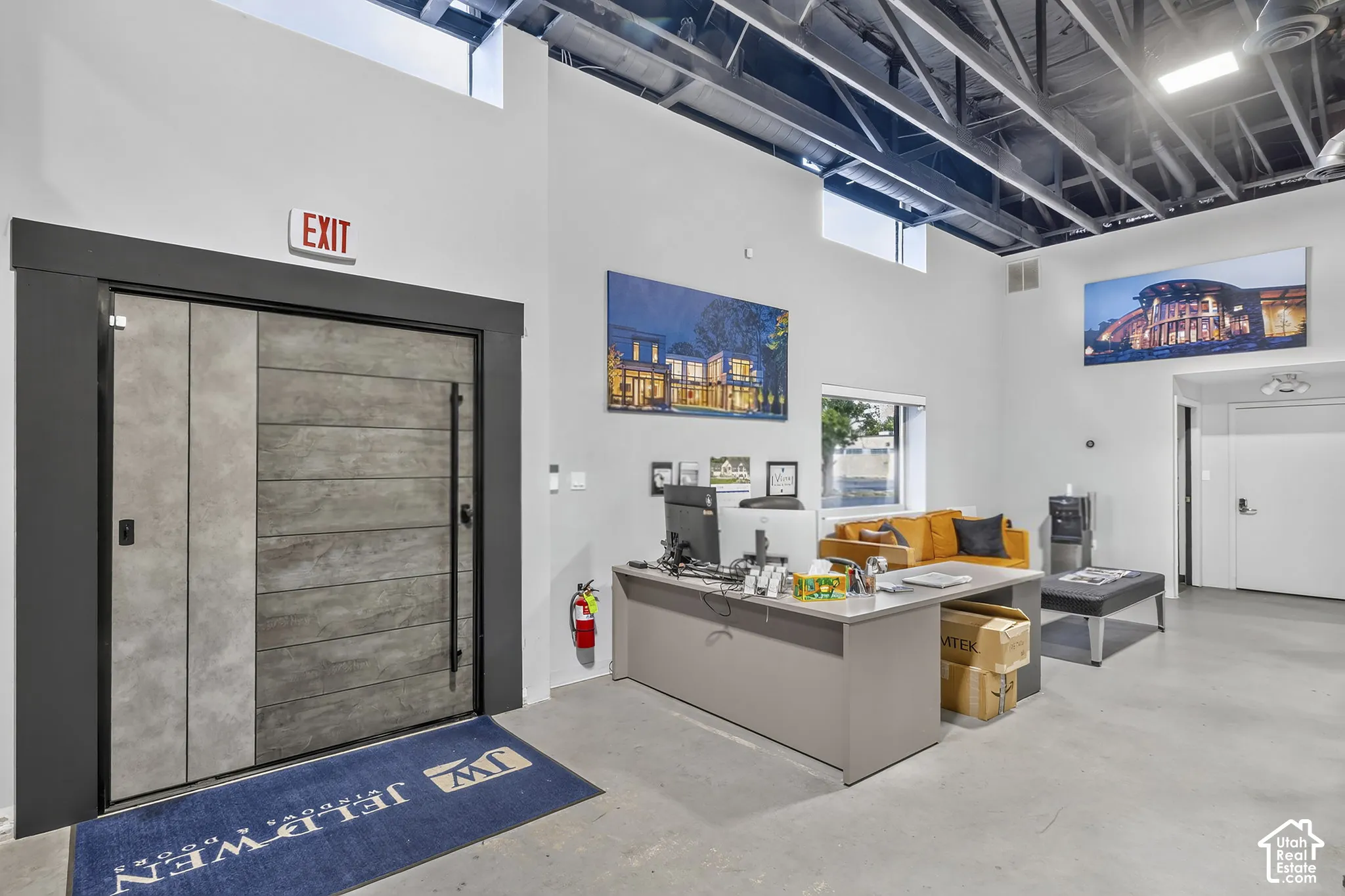 Industrial-style interior featuring an exposed ceiling, polished concrete flooring, clerestory windows, and a modern entrance door with a vertical pull handle and paneled finish