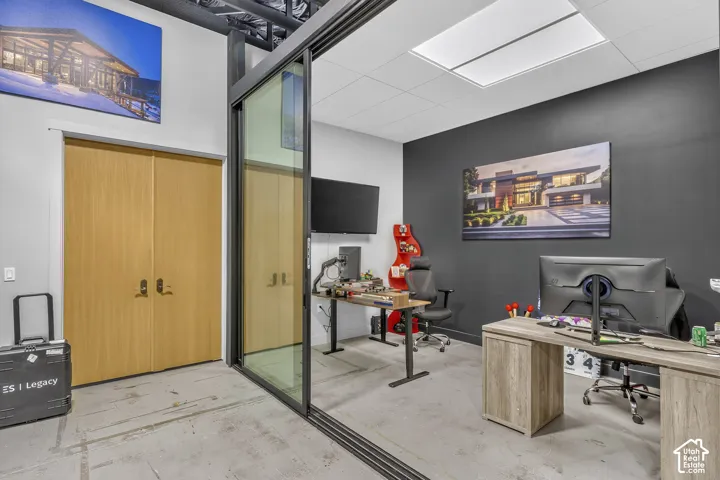 Glass sliding partition with a dark metal frame, double wood-veneer doors, exposed ceiling structure, recessed square lighting, and a charcoal-toned accent wall