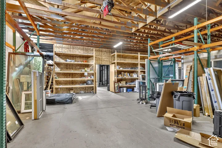 Industrial space featuring high vaulted ceilings with exposed wood trusses, concrete flooring, and built-in metal shelving units