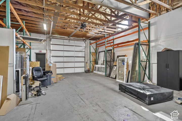 Industrial warehouse space featuring high vaulted ceilings with exposed wood trusses, concrete flooring, and a large sectional roll-up door