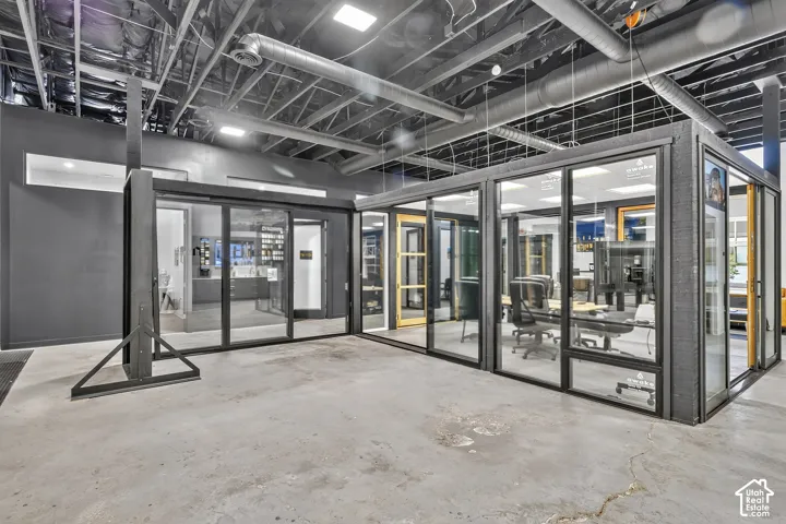 Industrial-style interior featuring an exposed ceiling with open ductwork, polished concrete flooring, and modular glass-paneled enclosures with black metal framing