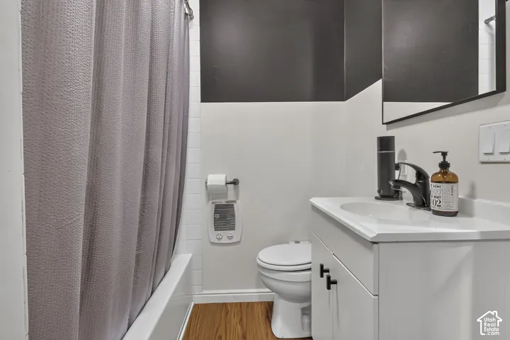 Bathroom featuring a white vanity cabinet with matte black hardware, integrated sink with a matte black faucet, wall-mounted mirror with a black frame, wood-finish flooring, and a subway-tiled shower surround