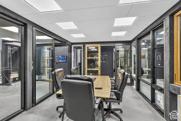 Polished concrete flooring, expansive glass wall partitions with black frames, recessed square ceiling lighting, and natural wood trim accents