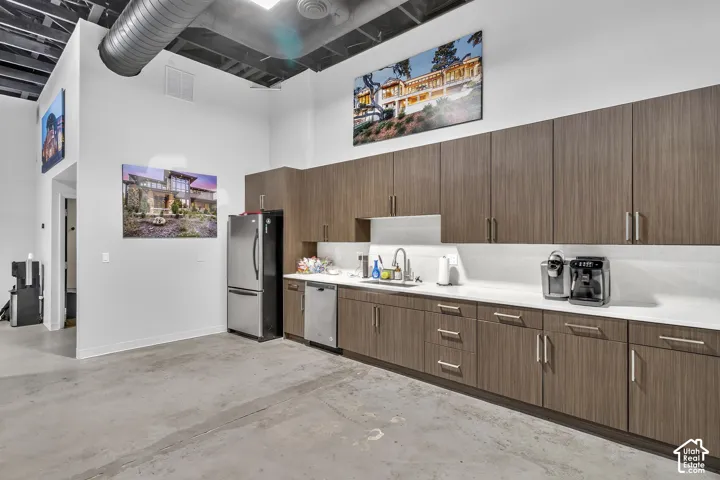 Custom cabinetry with wood-finish veneer, polished solid-surface countertops, integrated stainless steel appliances, exposed ductwork, and sealed concrete flooring