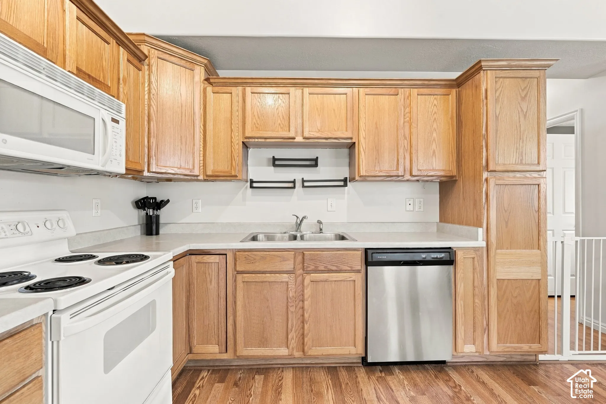 Kitchen featuring natural wood cabinetry, stainless steel dishwasher, white range with over-the-range microwave, double-basin sink, and wood-finish flooring