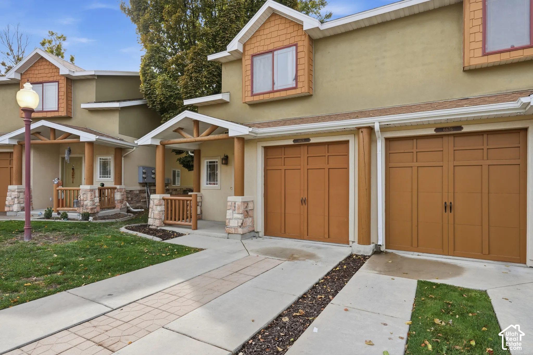 Exterior facade featuring multi-tone stucco, decorative shake siding, arched carriage-style garage doors, covered porches with wood railings, and stone-accented columns