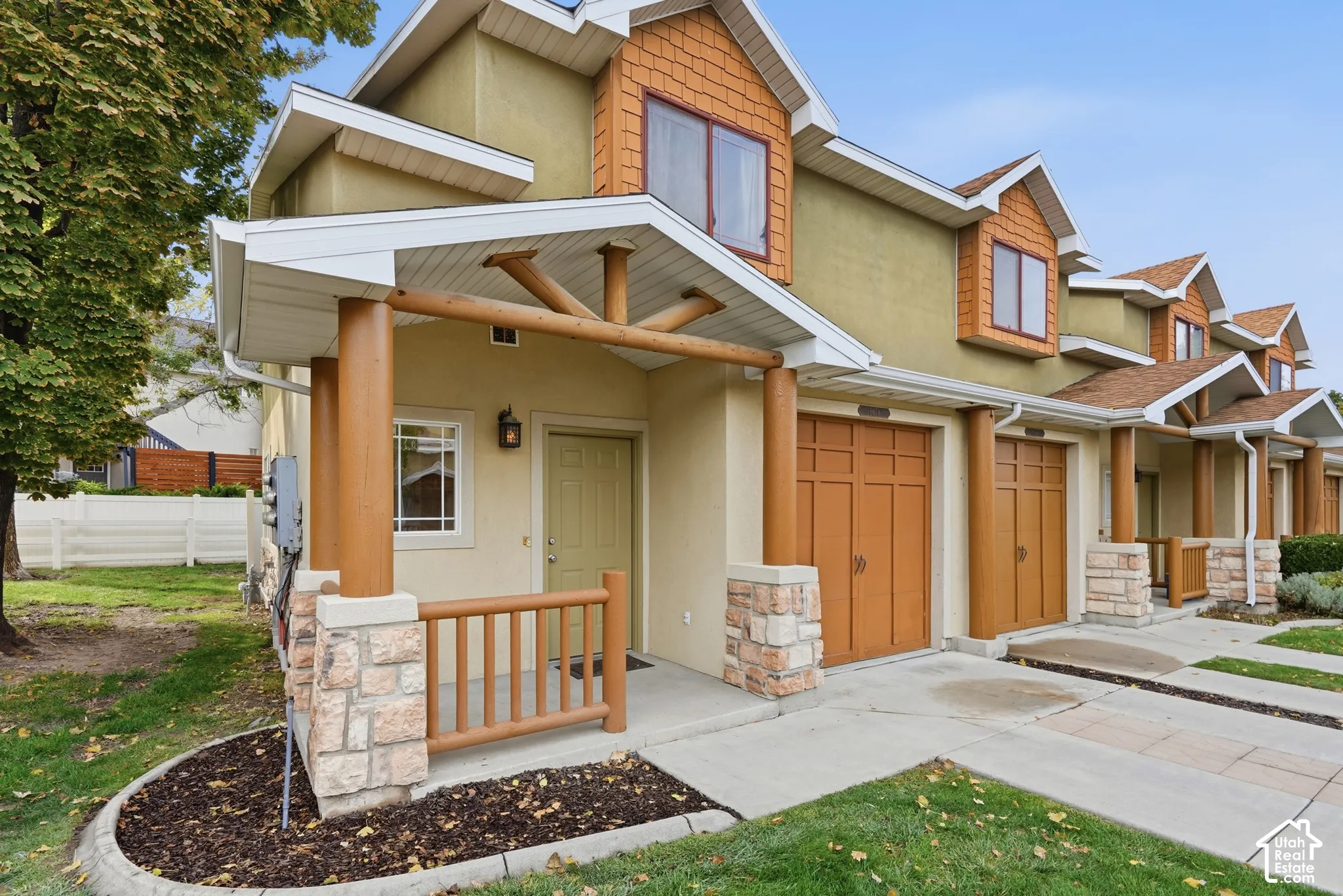 Exterior facade featuring rustic timber-style porch supports, stacked stone pillar bases, cedar-toned shingle accents, and attached garage doors