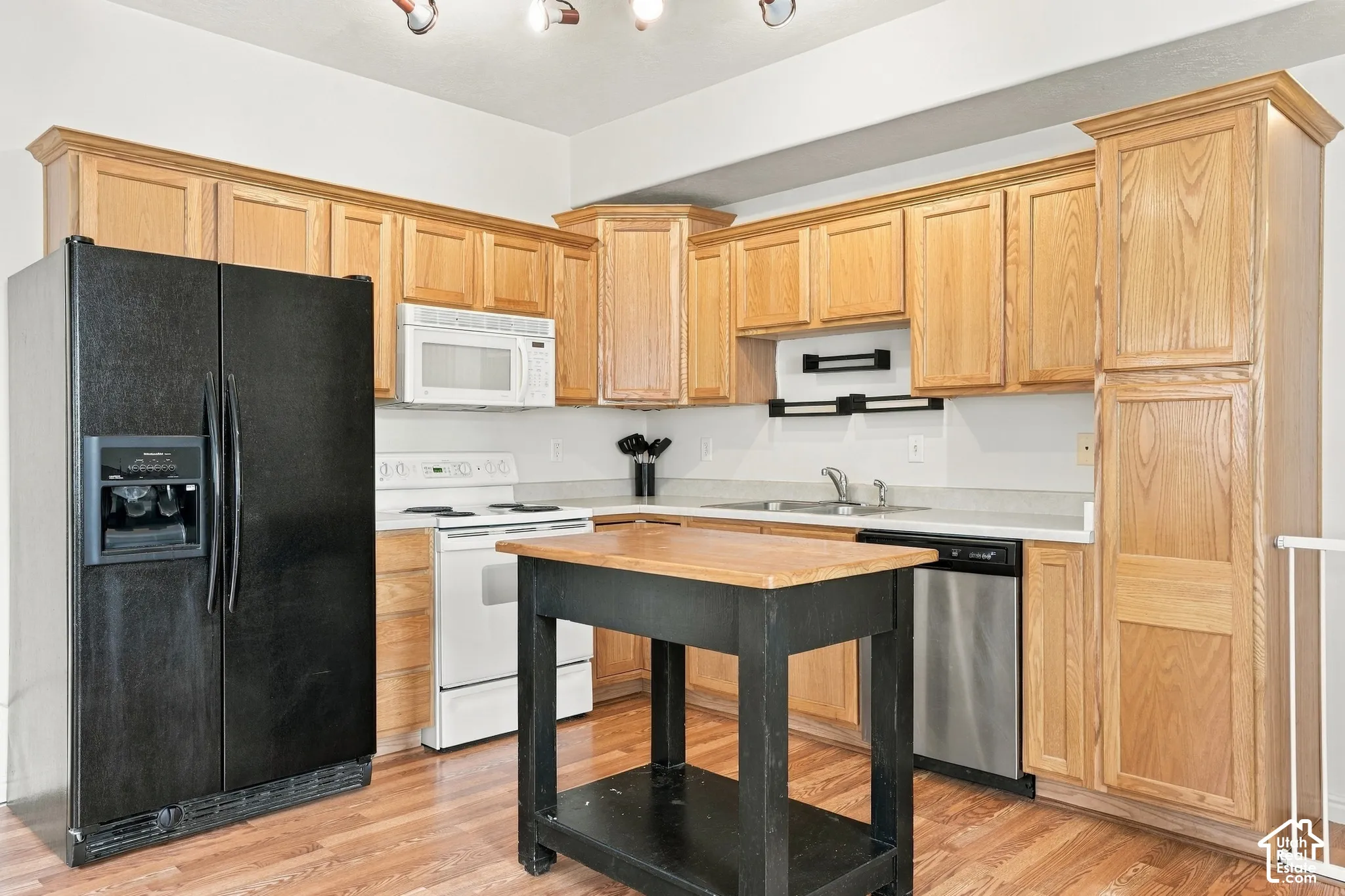 Kitchen featuring natural wood cabinetry, wood-finish flooring, white appliances, and a stainless steel dishwasher