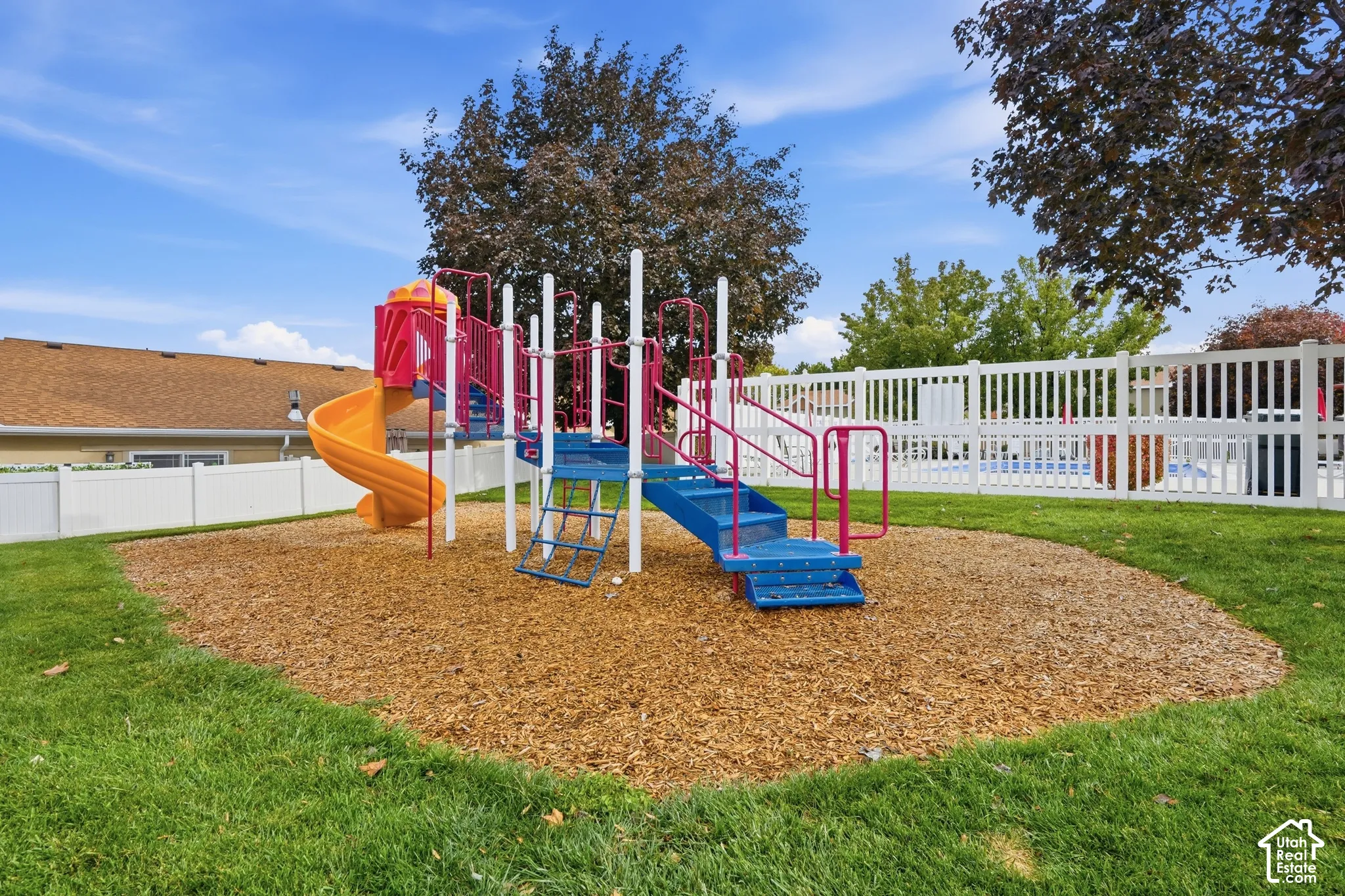 Outdoor recreation area featuring a built-in playground structure, wood-chip ground cover, manicured lawn, and perimeter privacy fencing