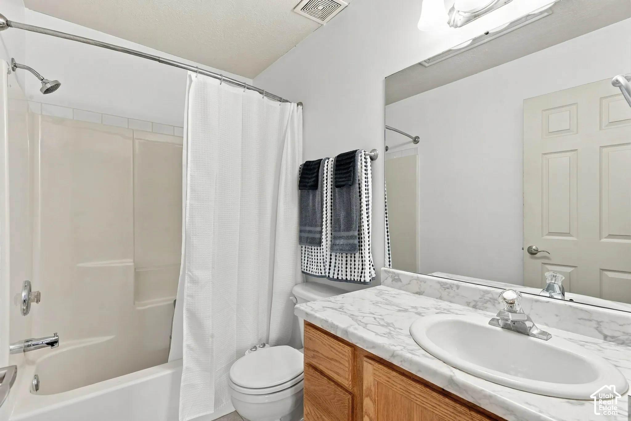 Bathroom featuring a vanity with a stone-patterned countertop, an oval drop-in sink, wooden cabinetry, and a full-width wall mirror