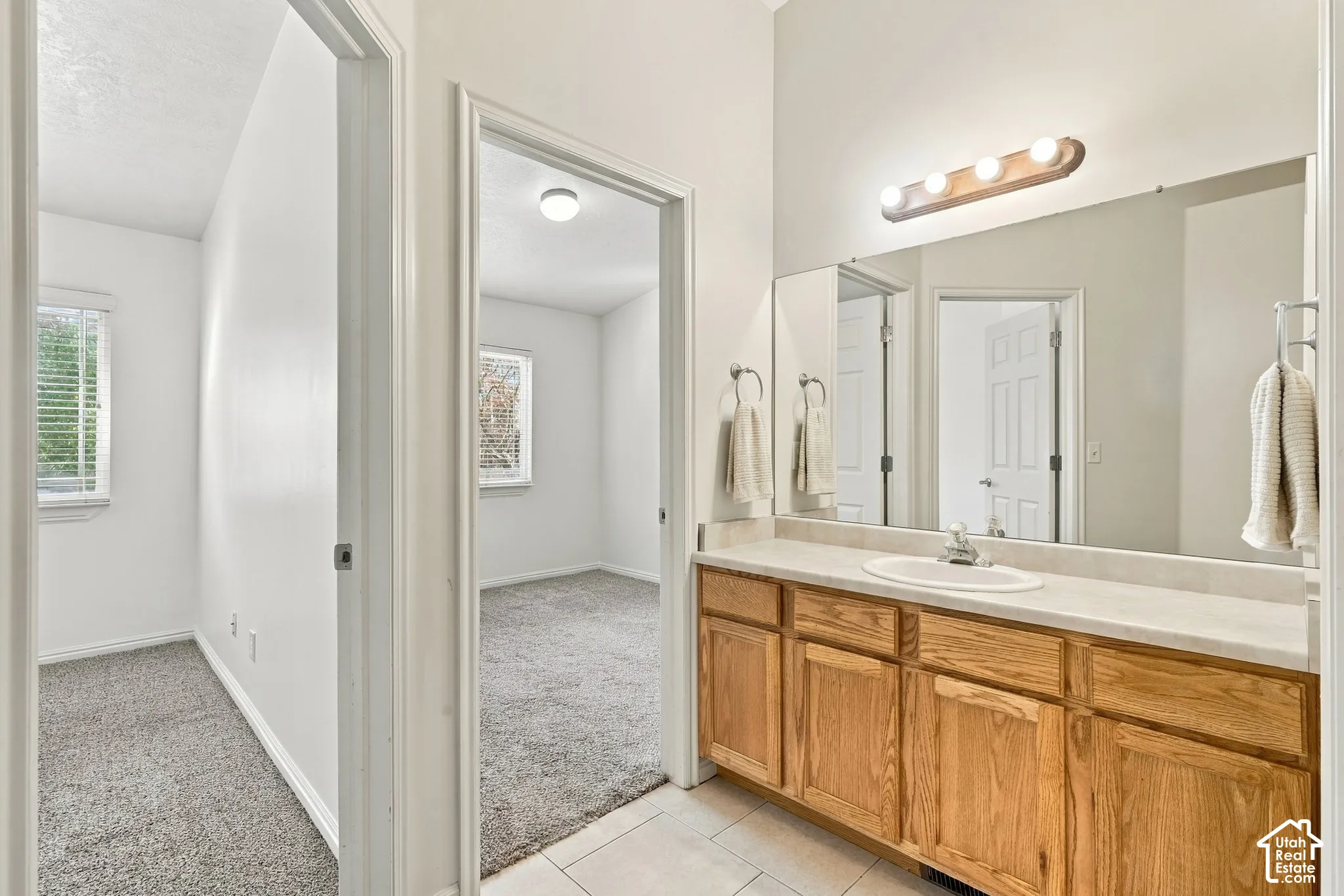 Bathroom featuring a wood-finish vanity with a stone-composite countertop, an integrated oval basin, a large wall-mounted vanity mirror, and a multi-light fixture