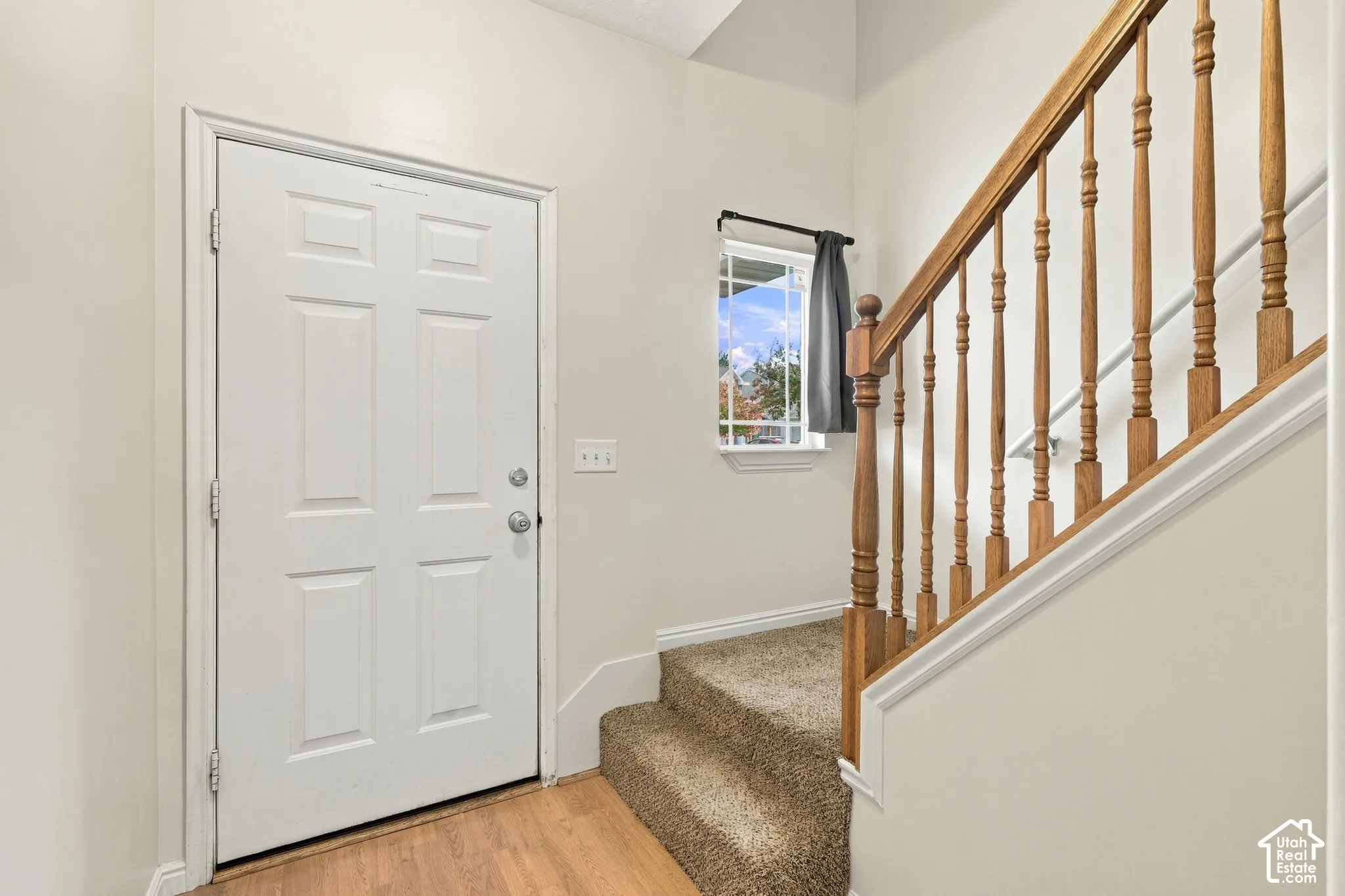 Entryway featuring a solid panel front door, wood-finish flooring, staircase with wood balusters and handrail, and wall-mounted window