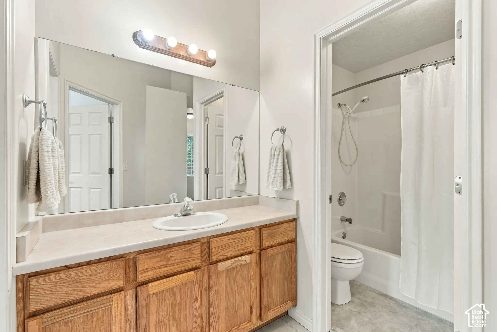 Bathroom featuring an oak vanity with a neutral solid-surface countertop, an integrated oval sink, a wall-to-wall mirror, and a tub-shower combination
