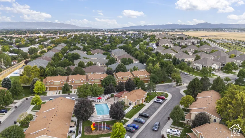 Aerial view of a residential community featuring a fenced swimming pool, playground area, paved streets, and mountain backdrop