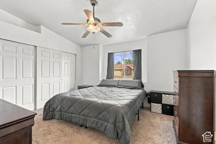 Bedroom featuring a vaulted ceiling, ceiling fan with integrated lighting, neutral wall-to-wall carpeting, and sliding panel closet doors