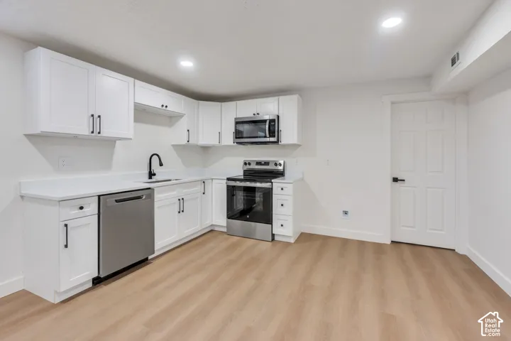 Kitchen featuring white shaker cabinetry, stainless steel appliances, solid surface countertops, matte black plumbing fixtures, and wood-finish flooring