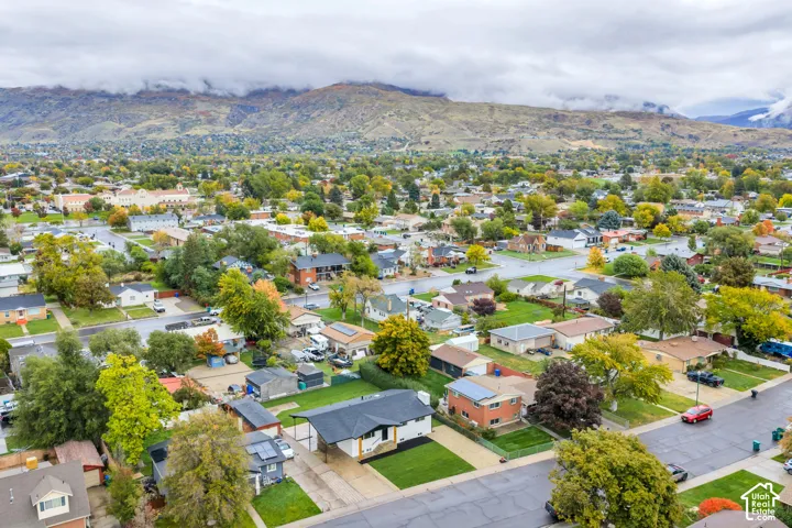 Aerial perspective showcasing a single-level residence with a covered carport, expansive lawn, mature landscaping, and a mountain backdrop