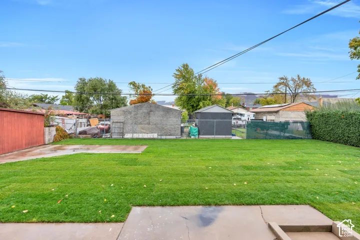 Expansive backyard featuring a level lawn, concrete patio, perimeter chain-link fencing, and two detached storage structures