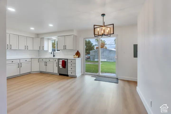 Kitchen featuring white cabinetry, subway tile backsplash, stainless steel dishwasher, wood-finish flooring, and a multi-light geometric chandelier