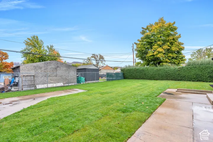 Expansive backyard featuring a level lawn, concrete patio, privacy hedge, and chain-link perimeter fencing