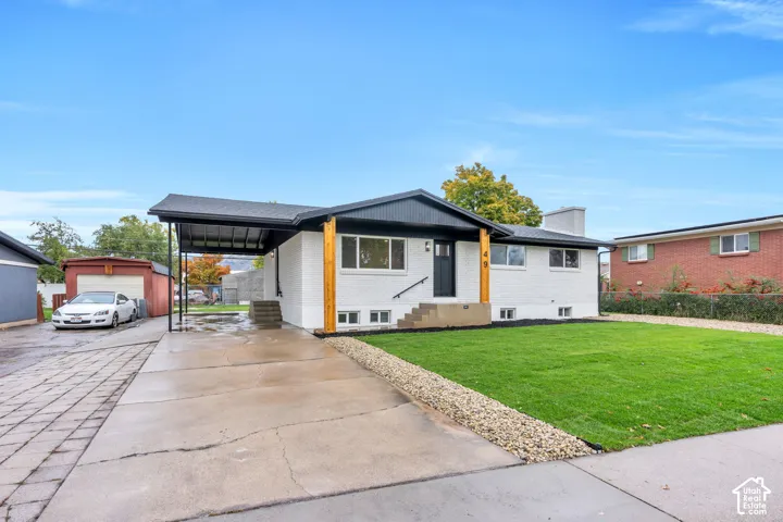 Single-story exterior featuring a white-painted brick facade, black roofline trim, exposed wood support pillars, an attached carport, and a front lawn with stone landscaping borders