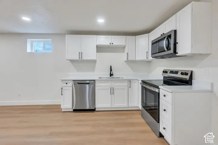Kitchen featuring white shaker-style cabinetry, quartz countertops, stainless steel appliances, a black pull-down faucet, and wood-finish flooring